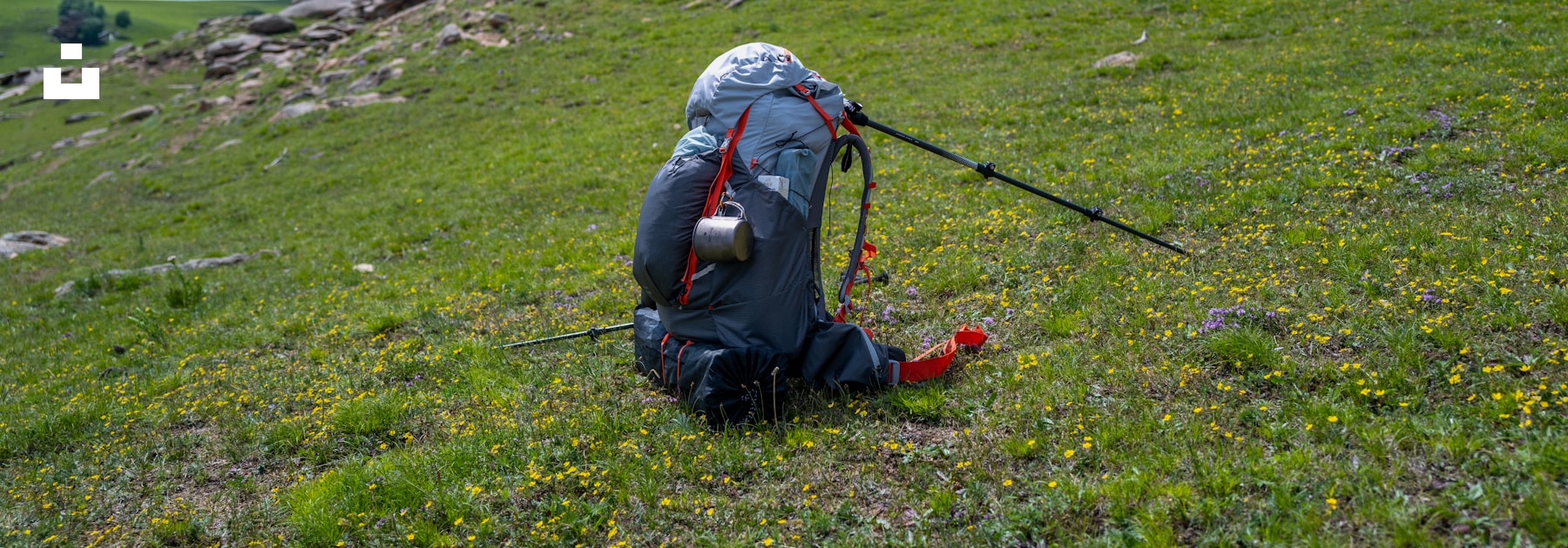 A backpack and hiking poles resting on an open hillside.